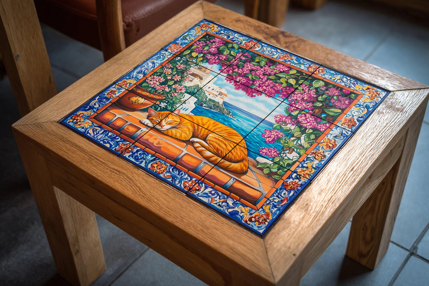 Ceramic tile mural with orange cat sleeping on terracotta tiles, view of a Mediterranean coastal village, bougainvillea and ornate floral border.