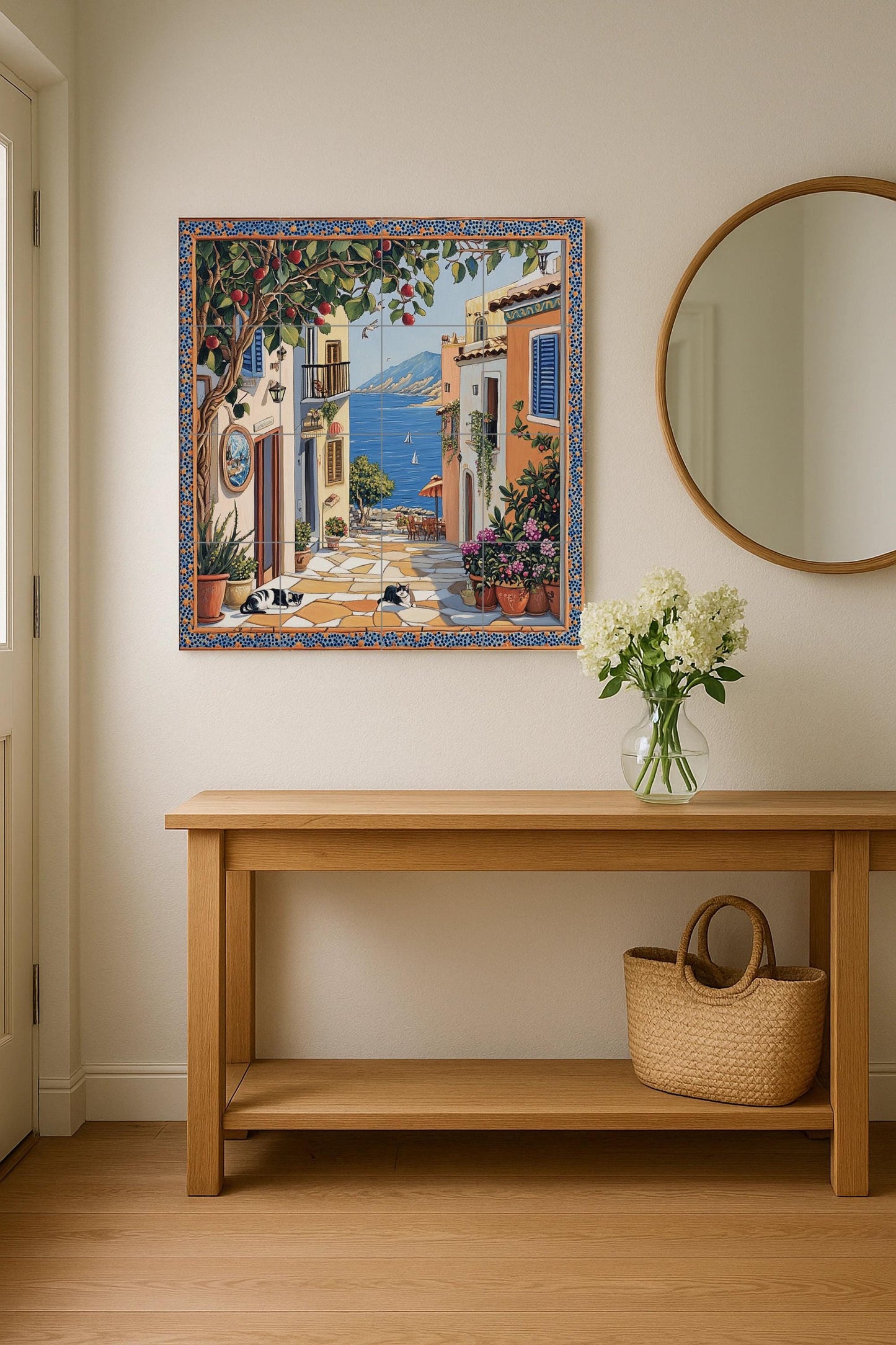 Ceramic tile mural with street scene of a coastal town, fruit tree, flower pots, houses by the sea and black and white cats resting on the pavement.