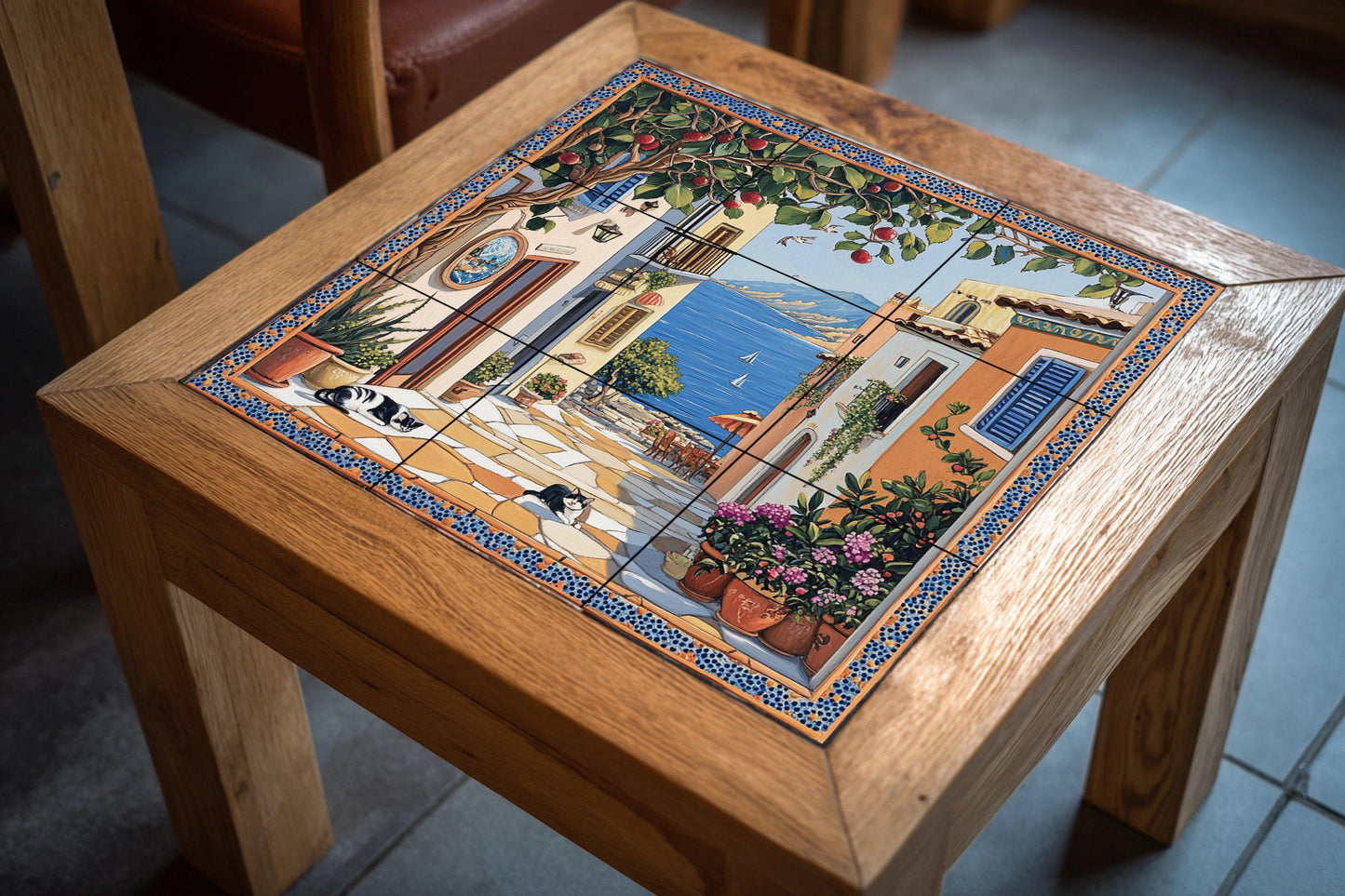 Ceramic tile mural with street scene of a coastal town, fruit tree, flower pots, houses by the sea and black and white cats resting on the pavement.
